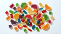 Colorful assorted gummy candies and fruit jelly sweets scattered on white background. Chewy treats in various shapes including bears, worms, and citrus slices.