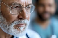 Close-up portrait of senior Caucasian male doctor with white beard and glasses showing confident expression, medical professional in clinical setting.