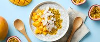 Tropical mango and passion fruit yogurt bowl with granola and coconut flakes on blue background, overhead flat lay for healthy breakfast and nutrition content.