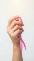 Female hand holding pink ribbon for breast cancer awareness campaign on light background with wedding ring.