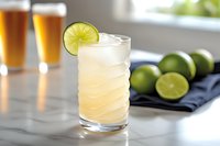 Fresh lime cocktail with ice in textured glass on marble counter, craft beer glasses and citrus fruits in background for summer refreshment and bar menu.