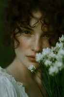Young woman with curly hair holding white wildflowers in natural outdoor setting with soft romantic lighting and dreamy atmosphere.