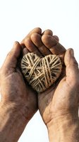 Elderly hands gently holding handmade rope heart symbol on white background representing love, care, protection and compassion in rustic natural style.
