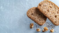 Fresh sliced whole grain sourdough bread with walnuts and caraway seeds on light blue textured background, top view composition for food photography.
