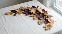 Autumn leaves scattered on white bedding near window creating cozy seasonal bedroom decor with natural fall foliage arrangement for home styling.