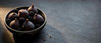 Fresh figs in a dark ceramic bowl on slate surface, ideal for food photography, culinary blogs, recipe websites, and restaurant menus.