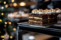 Decadent chocolate layered cake slice with nuts and cream filling displayed on cooling rack in warm bakery setting with golden bokeh lights.