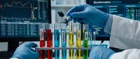 Scientist in blue gloves conducting laboratory research with colorful chemical solutions in test tubes against financial data screens background.