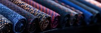 Rolled luxury fabric bolts in rich blue and purple tones showing detailed textile patterns and textures arranged in retail display, macro photography closeup view.