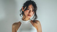 Young Asian woman with dark hair in updo wearing white halter top against neutral background, looking pensively at camera.