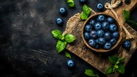 Fresh ripe blueberries in wooden bowl on rustic cutting board with mint leaves against dark textured background, top view with copy space.