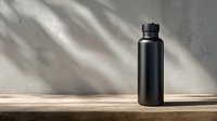 Matte black reusable water bottle standing on wooden surface with natural shadow overlay and concrete wall background, minimalist eco-friendly lifestyle concept.