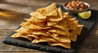 Golden crispy tortilla chips arranged on dark slate board with fresh salsa and lime wedge on rustic wooden background for Mexican cuisine and snack concepts.
