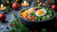 Hot stone bowl with rice, vegetables, sunny side up egg and fresh herbs served with Christmas decorations and burning candles in dark moody atmosphere.
