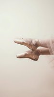 Dancer feet in satin pointe shoes performing ballet movement against soft beige background for dance and performing arts concepts.
