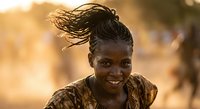 Young African woman with traditional braided hairstyle smiling warmly in golden sunset light, authentic portrait showcasing natural beauty and cultural heritage.