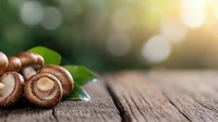 Fresh brown mushrooms with green leaves on rustic wooden table with natural sunlight and bokeh background for cooking and culinary designs.