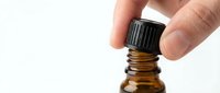 Hand opening amber glass bottle with black cap, essential oil or medicine dropper dispenser on white background for healthcare and wellness product packaging.