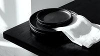 Stacked black cookware with white cloth on dark surface, monochrome kitchen still life composition for culinary and home decor projects.