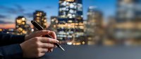 Professional businessman using smartphone in urban evening cityscape with illuminated skyscrapers and bokeh lights for business communication and networking.