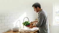 Caucasian male chef preparing fresh vegetables at kitchen counter with white subway tile backsplash and natural window light for cooking, meal prep, and culinary content.