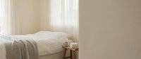Minimalist bedroom interior with unmade bed, soft natural lighting from window, neutral beige tones creating calm peaceful atmosphere for rest and relaxation.