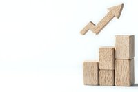 Wooden blocks arranged as ascending stairs with upward arrow symbol floating above on white background, representing growth and success in business.
