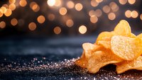 Orange heart-shaped gummy candies dusted with sugar crystals on dark surface against blurred golden bokeh lights background, sweet dessert concept.