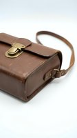 Vintage brown leather satchel bag with brass buckle and adjustable strap isolated on white background for fashion and accessory design projects.