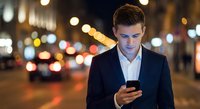 Young professional businessman using smartphone on city street at night with bokeh lights background for business communication and urban lifestyle.