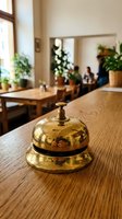 Golden brass service bell on wooden counter in cozy cafe interior with warm natural lighting and plants for hospitality and customer service concepts.