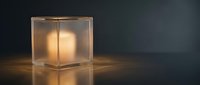 Frosted glass cube lamp with warm glowing light inside, casting soft illumination on dark surface, modern minimalist design for interior decor and lighting concepts.