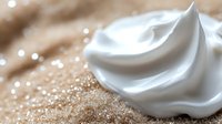 White cream swirl with golden glitter sparkles on warm beige background for cosmetic skincare beauty product advertising and luxury spa treatments.