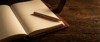 Open notebook with copper pen on rustic wooden desk creating warm atmospheric workspace for writing, journaling, planning and creative projects.