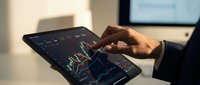 Professional businessman analyzing financial data and stock market charts on tablet device in modern office environment for investment decisions.