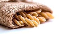 Uncooked pasta penne in burlap sack on white background, raw Italian food ingredients for cooking traditional Mediterranean cuisine.