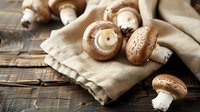 Fresh brown mushrooms on rustic linen napkin against dark wooden background, natural light creates moody atmosphere for food photography and culinary design.