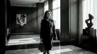 Professional businesswoman walking through modern office lobby with contemporary art sculptures and natural lighting from large windows.