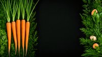 Fresh orange carrots with green tops arranged on dark background with copy space, organic vegetables for healthy eating and cooking.