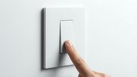 Hand pressing a white light switch on a clean white wall, turning power on or off in a modern home interior setting.