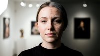 Young Caucasian woman with half face aging effect showing time passage concept in modern gallery interior for beauty and skincare campaigns.