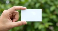 Hand holding blank white business card against blurred green nature background for mockup and branding design projects.
