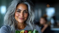 Smiling middle eastern woman with silver gray hair holding fresh organic produce in modern kitchen setting. Healthy lifestyle and wellness concept.