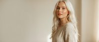Young blonde Caucasian woman in beige sweater looking away thoughtfully in soft natural light. Minimalist portrait for lifestyle and fashion content.