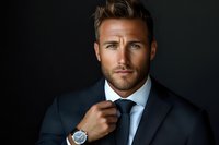 Confident Caucasian businessman in dark suit adjusting tie, wearing luxury watch against dark background. Professional portrait with dramatic lighting.