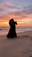 Romantic couple dancing on beach at sunset with dramatic orange and pink sky reflecting on ocean waves creating intimate silhouette moment.