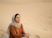 Young Middle Eastern woman wearing traditional hijab and rust-colored tunic, sitting in desert sand dunes, gazing thoughtfully into distance during golden hour light.