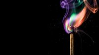 Colorful flame burning on wooden match stick with vibrant purple, green and orange smoke swirls against black background for creative design projects.