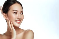 Young Asian woman with glowing healthy skin touching face gently while smiling. Natural beauty and skincare concept against light background.