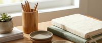 Minimalist wooden desk with bamboo pencil holder, stacked textured notebooks, ceramic bowls, and succulent plant in soft natural light.